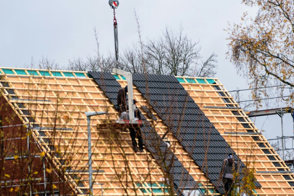 Dakwerkers leggen pannen op een nieuw dak, een kraan brengt de pannen naar boven