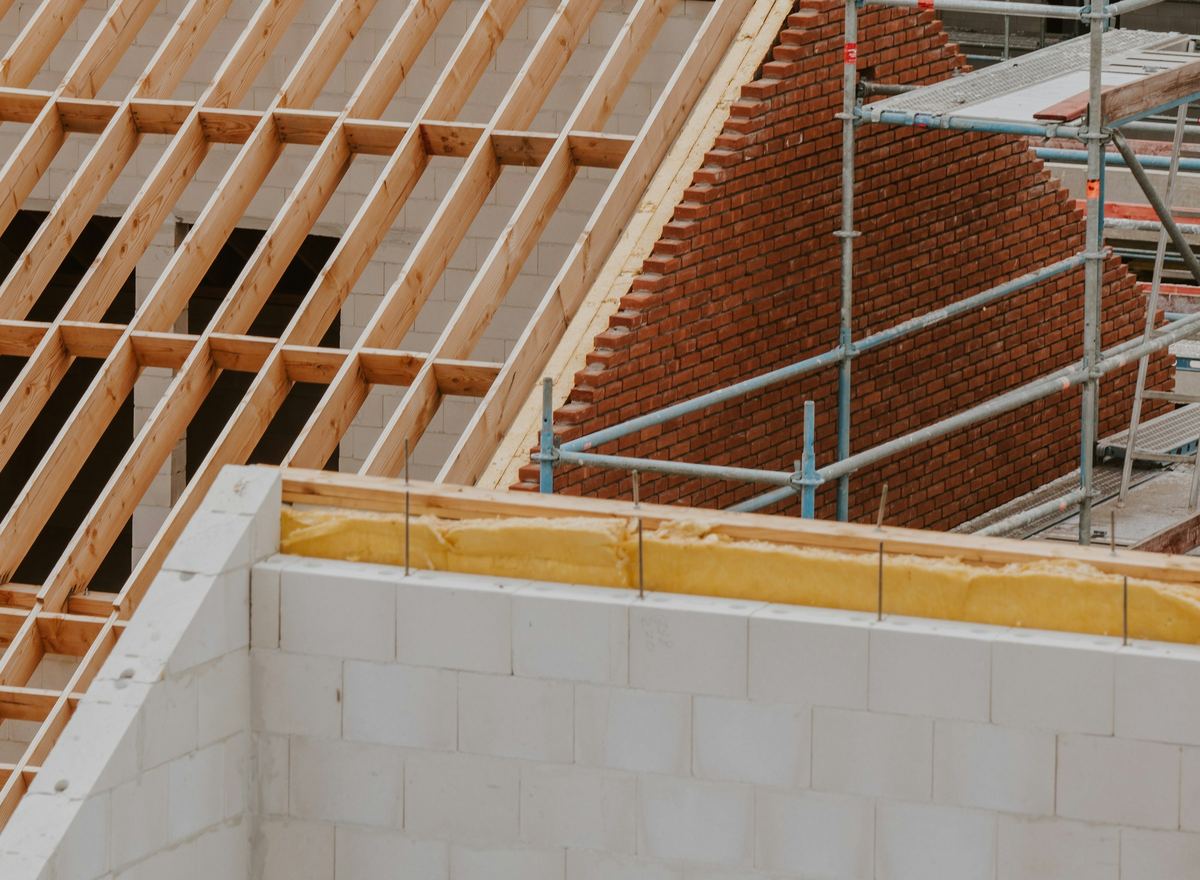 Nieuwbouw in opbouw: houten dakspanten op gemetselde muren, met een stelling ernaast